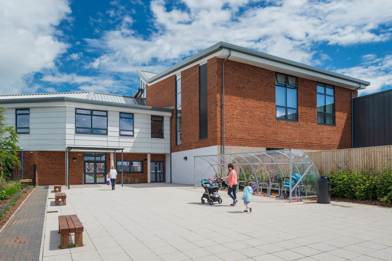 Entrance to a secondary school. A woman with a pushchair is walking towards the doors.