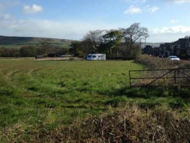 Field with a caravan parked at the far end of it.