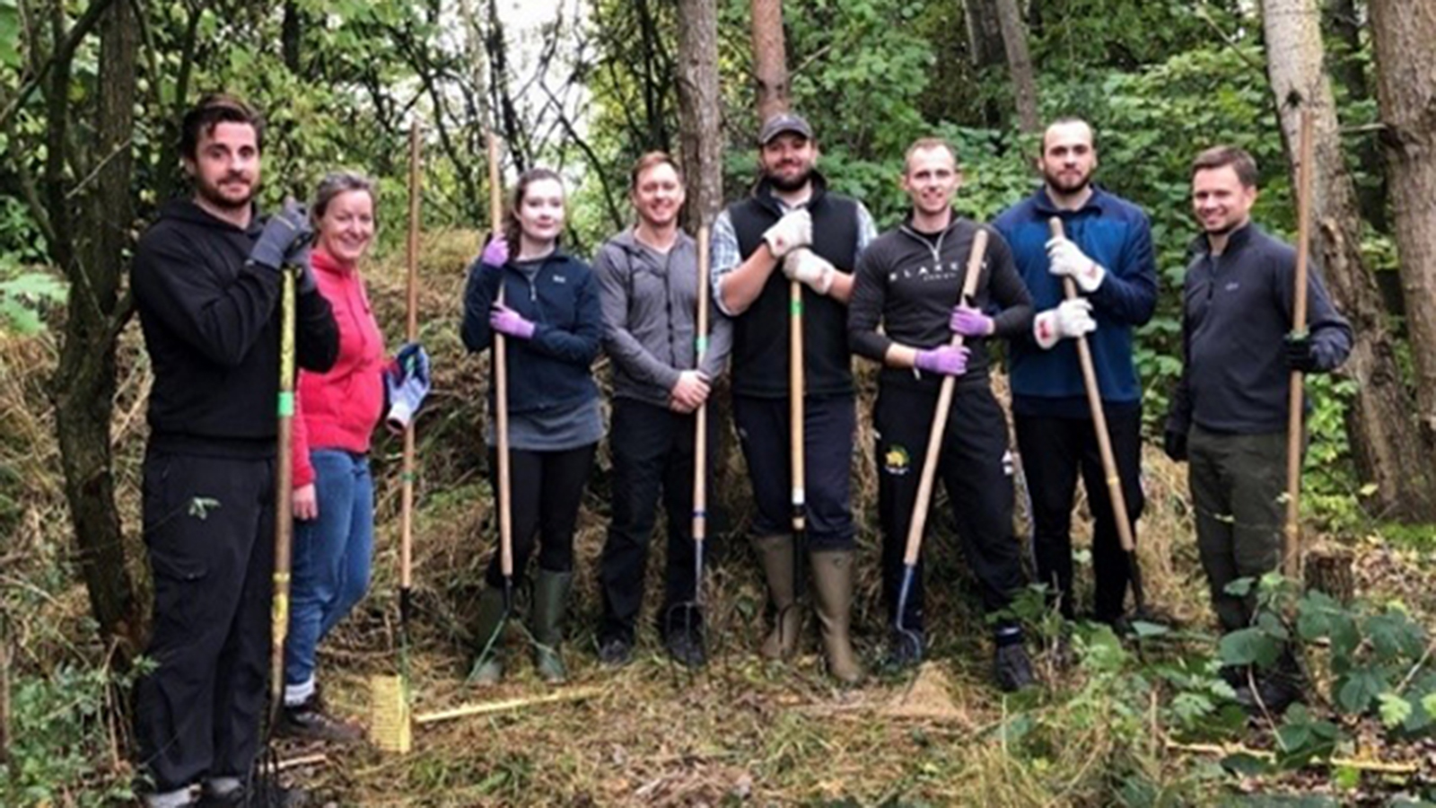 A group of people with various gardening tools such as spades, pitchforks and hoes.