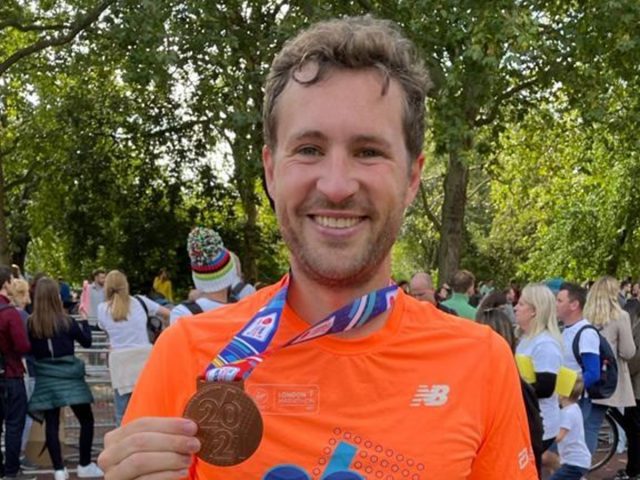 Man wearing running gear holding up medal with 2021 embossed on it.