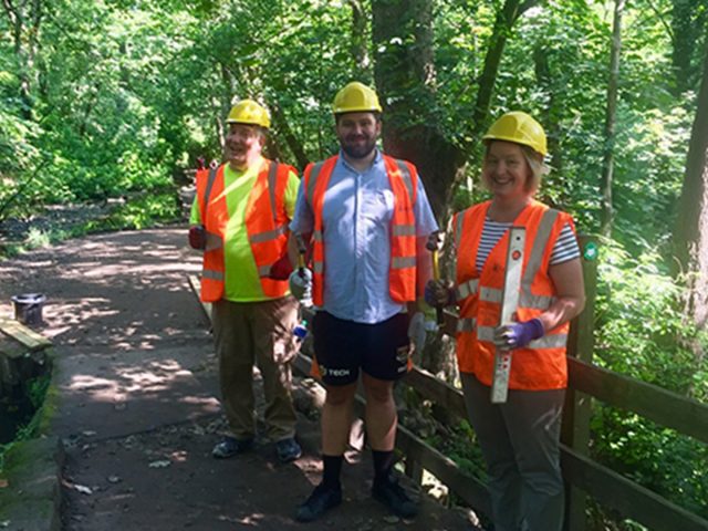 Volunteers in hi-vis and hard hats working in a wooded path.